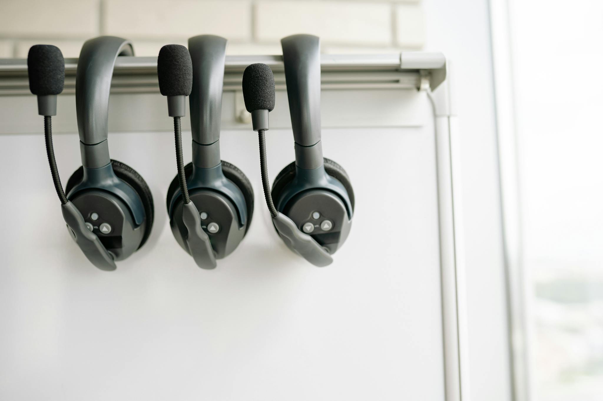 Three black headsets neatly organized on a whiteboard hook, emphasizing tech and communication.